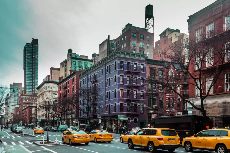 View of New York City street with yellow cabs and purple and red brick apartment buildings in background